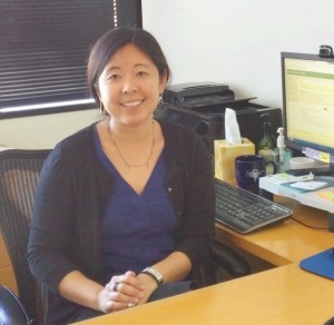 Photo of Amy Kaizuka in her office, seated at her desk with a computer screen behind her